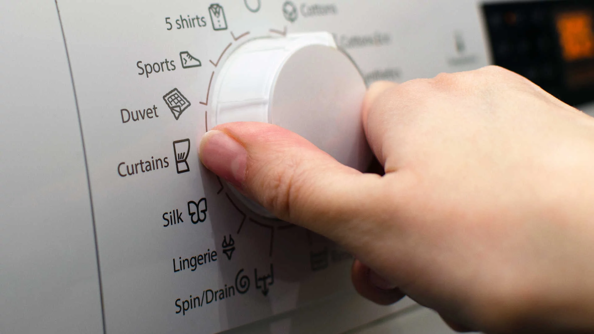 Hand turning the dial on washing machine settings