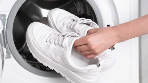 Image Alt Text Washing shoes at laundromat – person pulling clean shoes out of washing machine