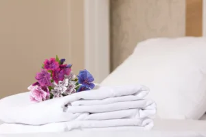 Folded towels on a made bed with a beautiful arrangement of flowers